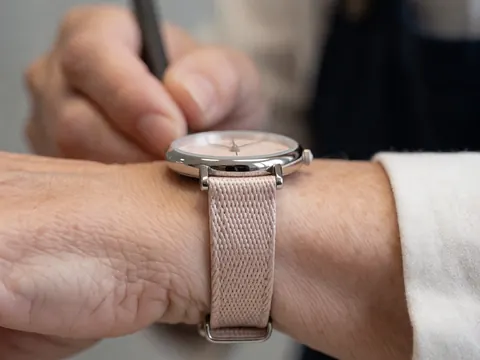 Fermeture de montre avec bracelet en tissu rose sur le poignet d'un adulte, main écrivant, fond flou. Détail d'une montre féminine avec bracelet en tissu rose et lunette polie, idéal pour la joaillerie.