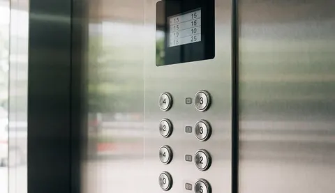 Panneau de contrôle moderne avec boutons ronds et écran digital affichant les étages, flou en arrière-plan pour services techniques.