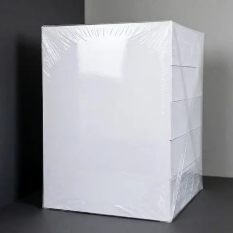 Une pile de papier A4 blanc enveloppée dans un film plastique transparent sur fond gris, produit de papeterie pour bureau ou école.