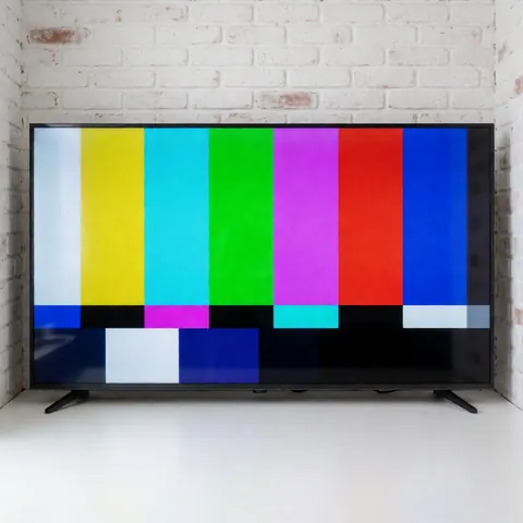 Grand téléviseur montrant une image de test de couleur sur un fond de mur de briques blanches peintes, illustrant la qualité d'image après réparation.
