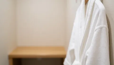 Linge blanc d'hôtel suspendu sur un porte-manteau avec un banc en bois flou en arrière-plan, créant une ambiance calme et neutre pour la préparation.