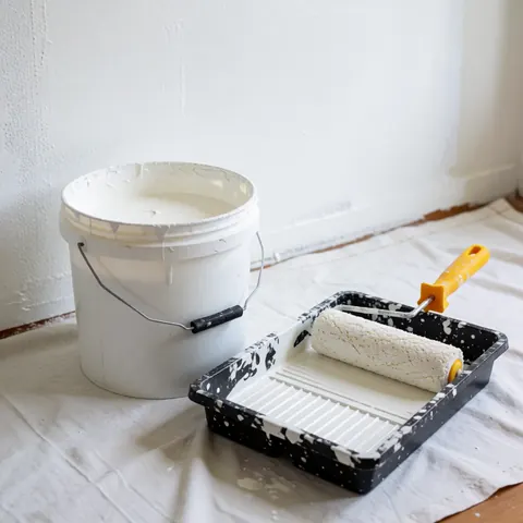 Un seau de peinture blanche accompagné d'un rouleau posé sur une tablette, le tout disposé sur un tissu blanc en vue d'une application murale.