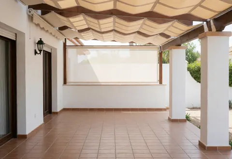 Patio extérieur avec auvent en bois et toile beige, sol en carreaux de terre cuite, murs blancs, éclairage naturel, idéal pour entreprise d'auvents.