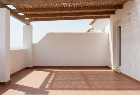 Patio résidentiel avec auvent en bois, sol en carreaux de terre cuite et murs en stuc, mettant en valeur l'installation d'un store pour la maison.