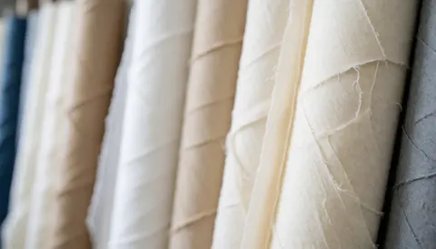 Fond composé de rouleaux de tissu en entreposage, offrant des couleurs neutres et une texture douce, idéal pour des textes sur la qualité des matériaux.