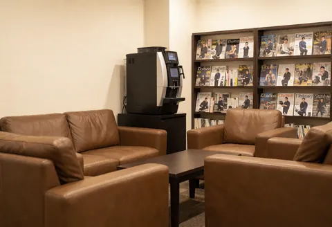 Espace détente équipé de canapés en cuir marron, d'une table basse et d'une étagère remplie de magazines de photographie, idéal pour se reposer et prendre un café.