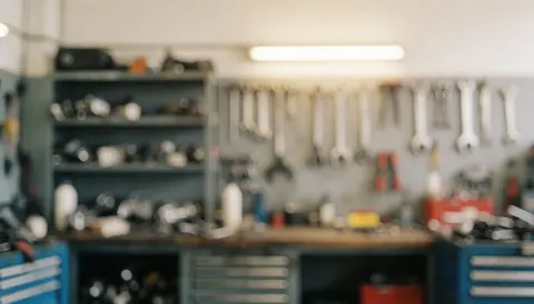 Fond d'atelier de réparation de moteurs avec outils suspendus, étagères à pièces et boîtes à outils, éclairage chaleureux et arrière-plan flou idéal pour du texte.