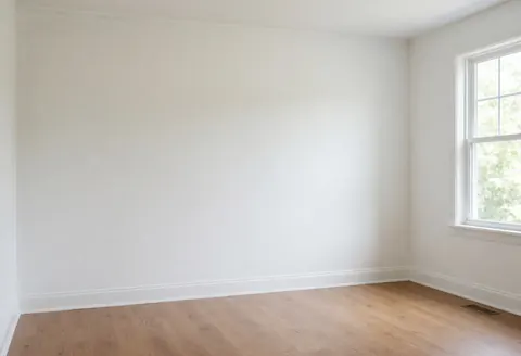 Salle de maison avec murs blancs fraîchement peints, sol en bois clair et lumière naturelle entrant par la fenêtre, idéal pour illustrer des services de peinture intérieure.