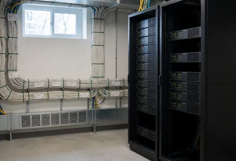 Salle de serveurs équipée de racks noirs, de câbles blancs étiquetés et de petites fenêtres. Idéale pour l'installation de systèmes de vidéosurveillance professionnelle.