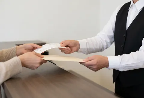 Mains d'un employé de hôtel tendant un document administratif à un client au premier plan avec un arrière-plan flou.