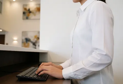 Mains d'un employé de réception utilisant un clavier devant un fond moderne avec des œuvres d'art sur les murs blancs dans un environnement professionnel.