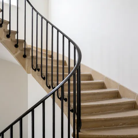 Vue de dessus d'un garde-corps en fer noir courbé sur un escalier en pierre beige avec murs blancs, idéal pour les installateurs d'escaliers.