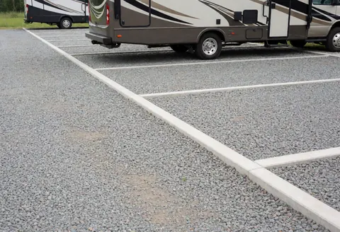 Vue d'un parking pour véhicules de loisirs avec des lignes blanches tracées sur le gravier, indiquant des emplacements de stationnement ordonnés.