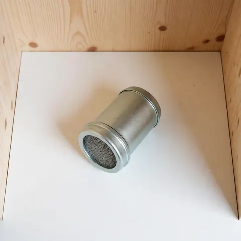 Filtre à gaz cylindrique en métal avec grille posé sur une boîte en bois, vue de dessus sur fond blanc, idéal pour les installations de gaz.