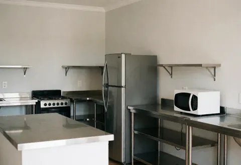Cuisine partagée d'auberge équipée d'un réfrigérateur, d'un micro-ondes, d'une cuisinière et de surfaces en acier inoxydable propres et bien rangées.