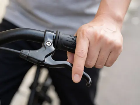 Gros plan d'une main tenant le guidon d'un vélo équipé d'un système de freinage, mettant en valeur la texture du grip et les détails mécaniques.
