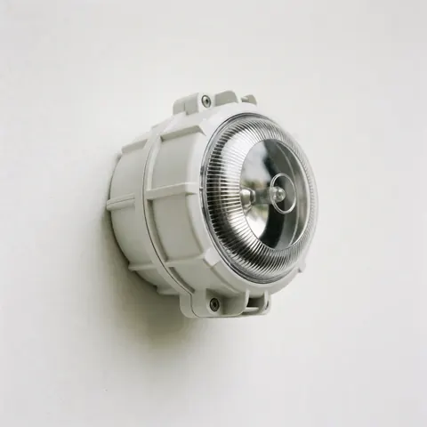 Sirène d'alarme extérieure blanche, robuste et résistante, fixée sur un mur blanc, avec une lentille transparente et un design industriel, idéale pour une utilisation en plein air.