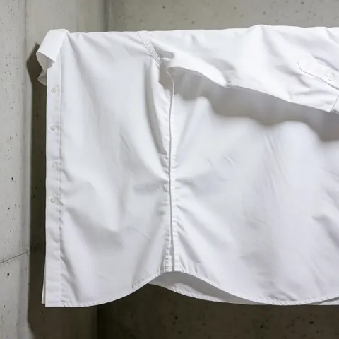Chemise formelle blanche suspendue sur un mur en béton, éclairage uniforme mettant en valeur la propreté de la réparation.