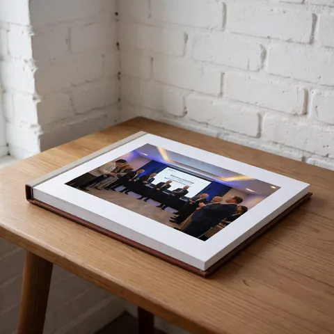 Album photo à couverture en cuir posé sur une table en bois dans une salle de réunion avec murs en briques blanches, évoquant un contexte professionnel.
