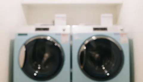 Arrière-plan flou de deux laveuses bleu clair dans une laverie, idéal pour illustrer des services de nettoyage et de blanchisserie en auberge de jeunesse.