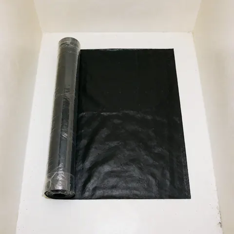 Rouleau d'étanchéité noir partiellement déroulé sur une surface blanche plane, prêt pour l'installation en construction commerciale.