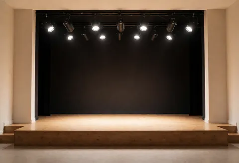 Scène de danse vide équipée de projecteurs et de murs beiges, prête pour des cours de danse professionnelle.