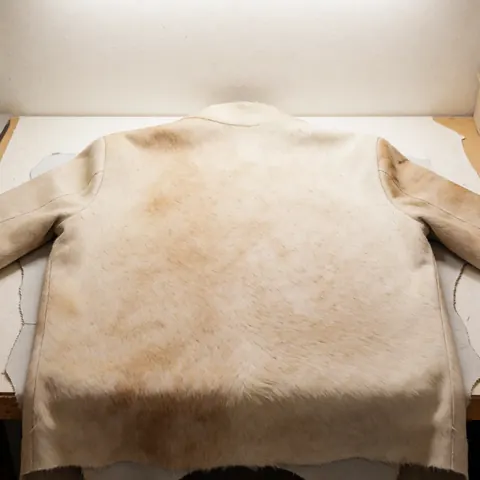 Coussin en cuir de vache avec texture naturelle posé sur une table de travail dans un atelier, éclairage lumineux et mur chaud en arrière-plan.
