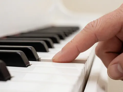 Gros plan d'une main adulte pressant une touche blanche de piano, avec un fond flou et une lumière douce, mettant en valeur la précision du geste.