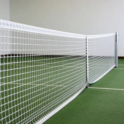 Filet de tennis blanc centré et tendu avec des poteaux argentés sur un sol vert, fond de mur blanc et éclairage professionnel pour installerur de courts de tennis.