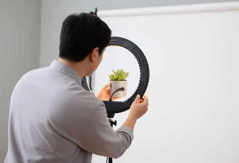 Un photographe professionnel règle une lumière annulaire autour d'une plante succulente dans un studio au fond blanc, illustrant un service de photographie macro en action.