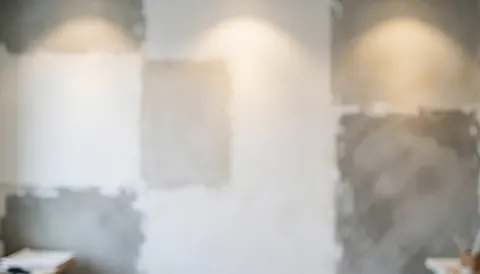 Fond de mur d'étude présentant des échantillons d'enduit blanc et gris, éclairage chaleureux et flou, idéal pour textes commerciaux.