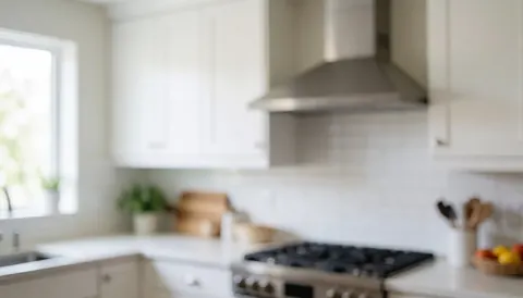 Cuisine moderne équipée d'une hotte extractrice en acier inoxydable, de placards blancs et éclairée par la lumière naturelle, idéale pour un fond textuel professionnel.