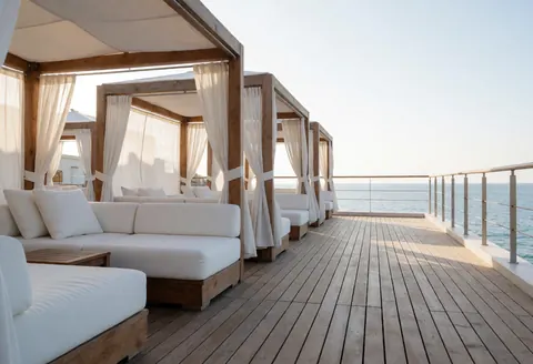 Terrasse surélevée dotée de cabanes en bois équipées de rideaux, accompagnée de canapés blancs offrant une vue imprenable sur la mer dans un cadre exclusif et ensoleillé.
