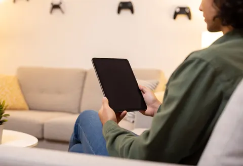 Une cliente attend dans une salle d'attente moderne avec une tablette. Le décor de jeux vidéo et l'éclairage créent une ambiance chaleureuse et professionnelle.