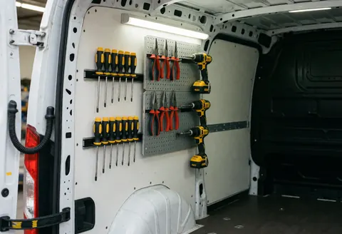 Intérieur d'une camionnette blanche avec outils comme tournevis, pinces et perceuses sur le tableau de bord et supports magnétiques, éclairé par lumière fluorescente.