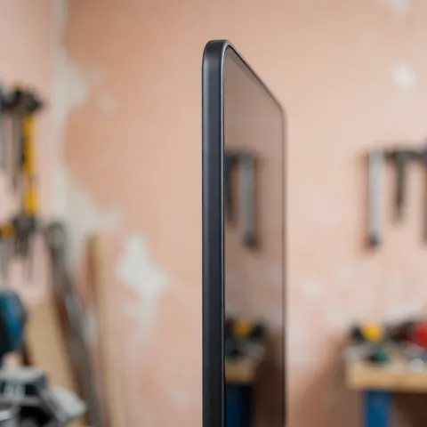 Nouvel écran de téléphone avec bord noir arrondi, vue latérale en atelier avec outils flous sur fond terracotta