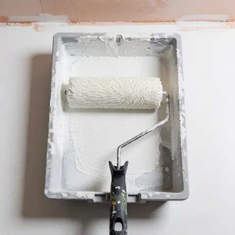 Un rouleau à peinture blanc saturé posé dans un bac en plastique gris, prêt pour l'application sur les murs. Idéal pour les entreprises de réparation.