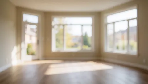 Salon vide et dégagé avec sol en bois, grandes fenêtres et lumière naturelle douce, idéal pour textes et projets de pose de sols.