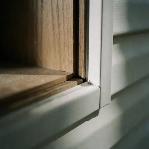 Gros plan sur la jonction entre un encadrement en bois et un profilé blanc en vinyle, mettant en valeur la texture naturelle du bois et la qualité de l'assemblage sous une lumière douce.