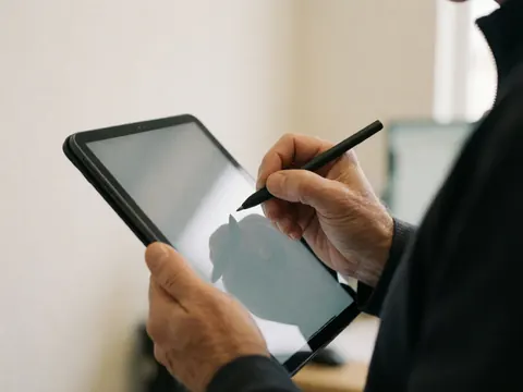 Gros plan d'une main adulte utilisant un stylet pour signer sur une tablette numérique dans un environnement de bureau moderne.