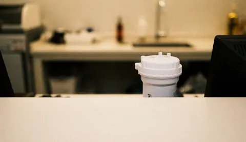 Un filtre à eau blanc posé sur un comptoir avec un arrière-plan flou d'atelier de réparation éclairage chaud et diffus idéal pour ajouter du texte.