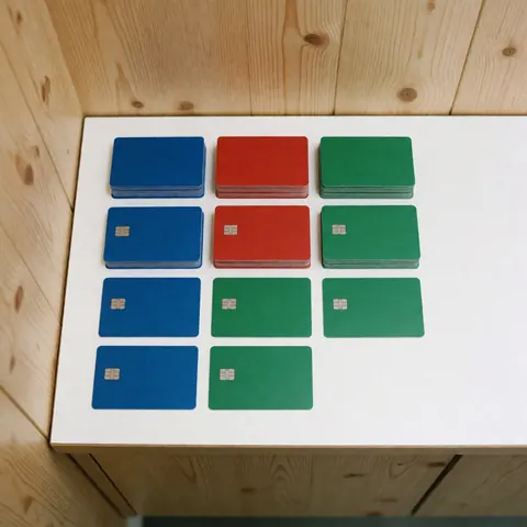 Des cartes de couleur bleue, rouge et verte sont alignées sur une surface blanche, avec des panneaux en bois en arrière-plan, sous un éclairage uniforme et professionnel.
