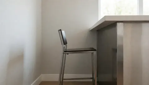 Chaise de bar avec structure métallique et assise noire, placée à côté d'un comptoir en métal poli dans un espace moderne aux murs gris.