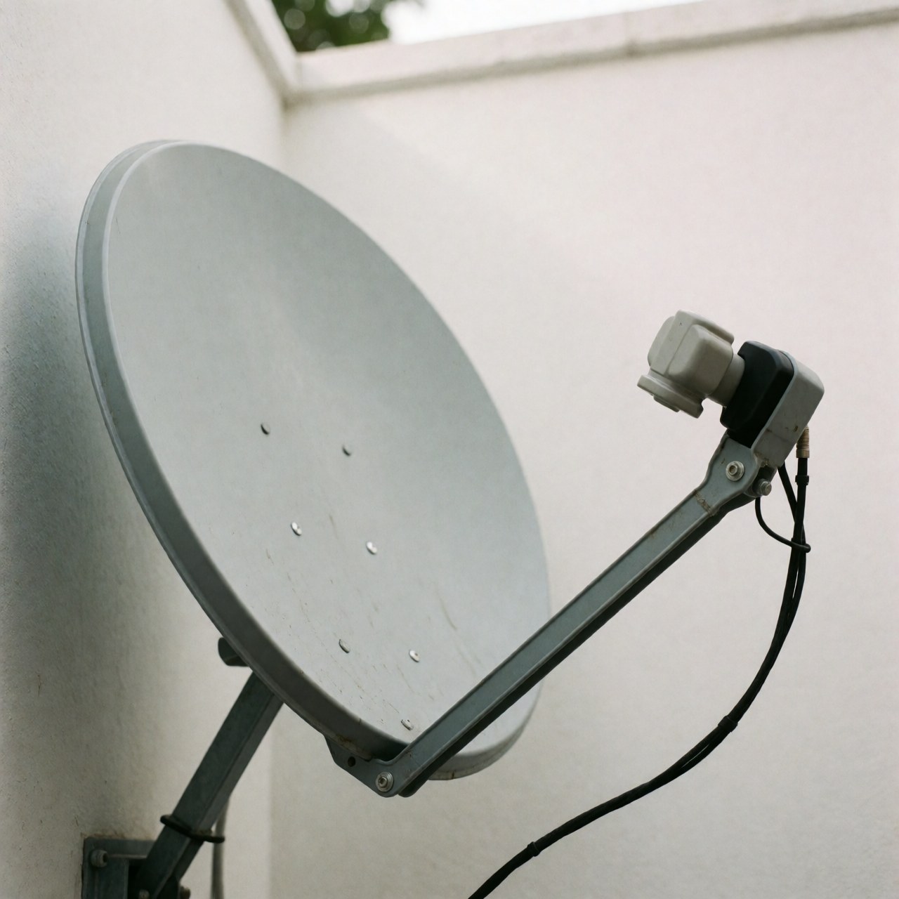 Installation professionnelle d'une antenne satellite sur un mur blanc avec câble et LNB visibles pour les entreprises de montage.