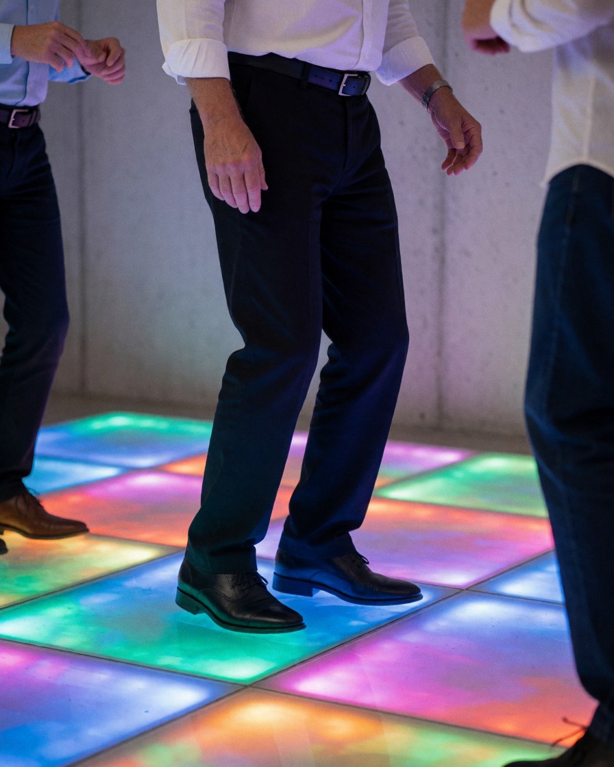 Pieds d'adultes sur un sol de salle d'événements avec des lumières LED changeantes, murs en béton et ambiance professionnelle vibrante.