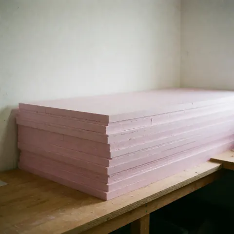 Piles de panneaux d'isolation thermique roses, matériaux pour l'isolation des fondations, posés sur un établi en bois dans un entrepôt aux murs blancs.