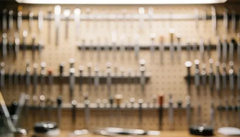 Fond d'atelier de horlogerie avec outils suspendus sur mur en bois, éclairage chaud et effet bokeh, idéal pour textes et logos.