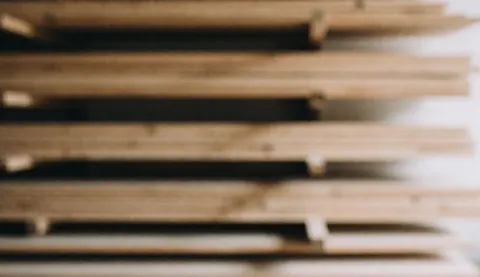 Fond d'atelier de menuiserie avec des planches de bois empilées et floues, éclairage doux et chaleureux, idéal pour les textes de services de design d'intérieur.