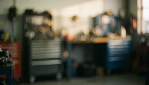 Fond flou d'un atelier de réparation avec des tiroirs à outils, des tables de travail et une lumière chaude, idéal pour les textes de services.