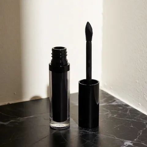 Flacon noir contenant un produit cosmétique liquide muni d'un applicateur, posé sur une surface en marbre sombre sous un éclairage latéral dramatique.